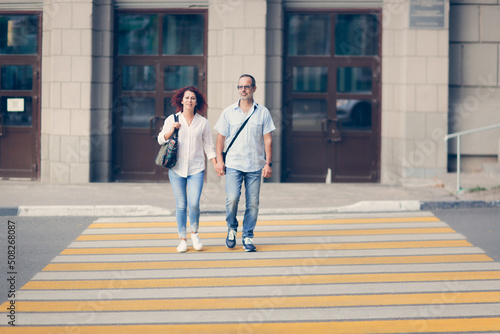 Cute middle aged european couple holding hands and crossing the road on a pedestrian crossing in the cities, summer walks and travel