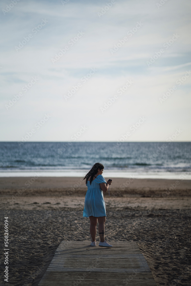 mujer de espaldas tomando fotos en la playa sobre camino de madera mujer de espaldas tomando fotos en la playa sobre camino de madera