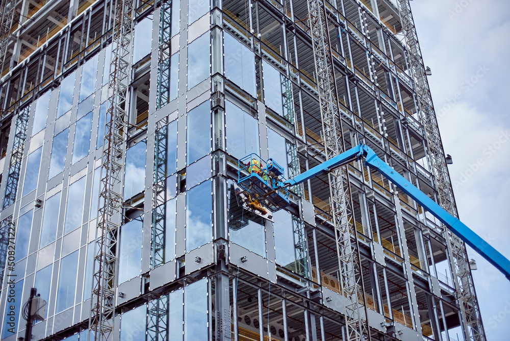 Installation of double-glazed windows from a crane, on a high-rise building. Construction of a skyscraper. Installation of windows on the glass building facade.