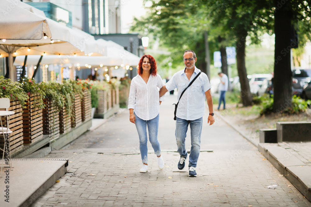 Cute European middle-aged couple hold hands and walk through the streets of the city, near the cafe, summer walks and travel