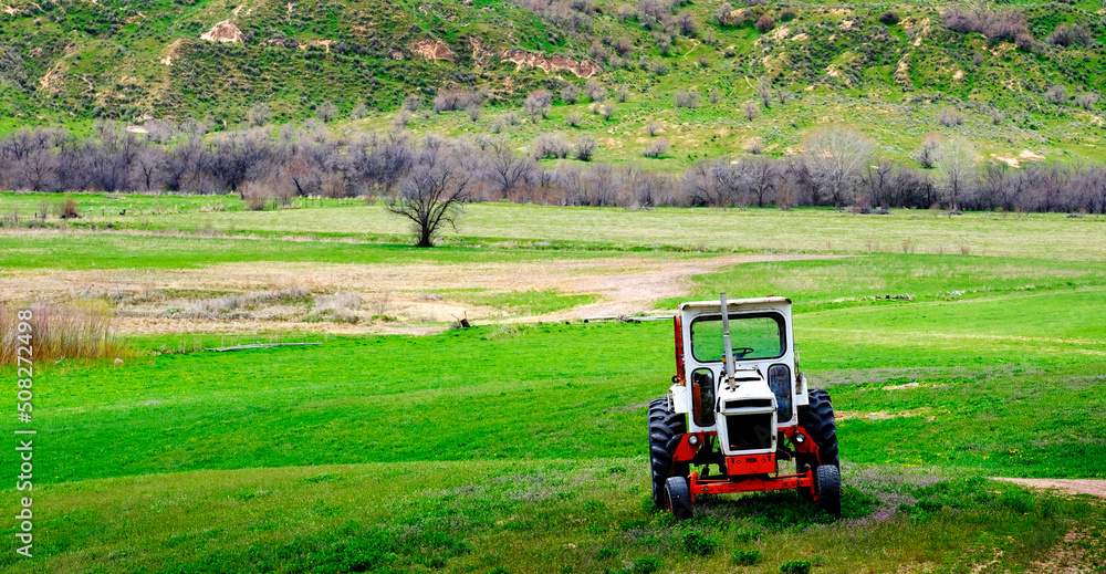 Fototapeta premium Old Tractor on Farm Field Green with Hills Mountains