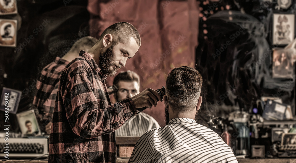 Bearded man in barbershop. Haircut concept. Man visiting hairstylist in barbershop. Barber works with hair clipper. Hipster client getting haircut. Hands of barber with hair clipper, close up