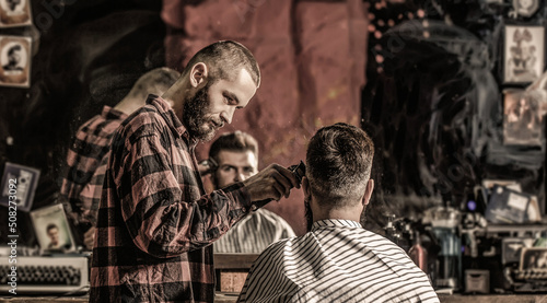 Bearded man in barbershop. Haircut concept. Man visiting hairstylist in barbershop. Barber works with hair clipper. Hipster client getting haircut. Hands of barber with hair clipper, close up