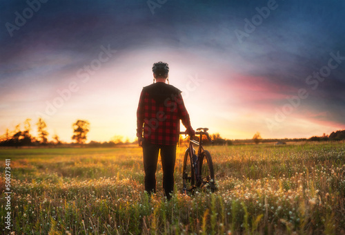 Cyclist in the field admires the beautiful sunset. Sport and travel concept.