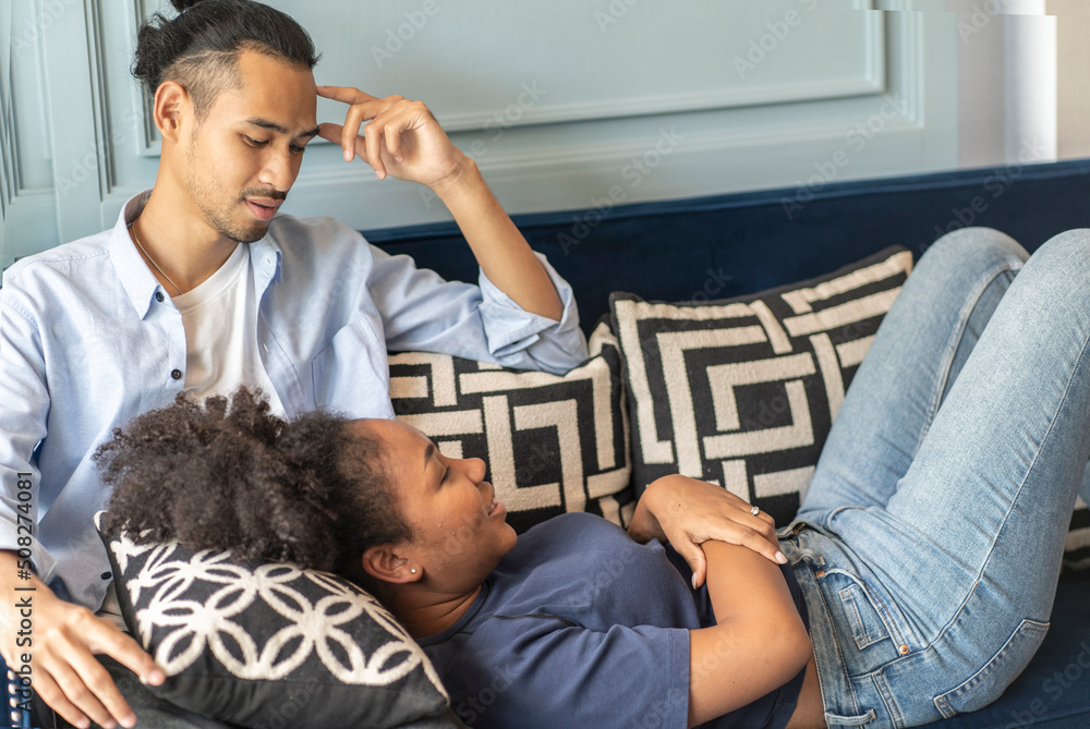 husband watches TV and an African-American wife rests on her lap on the sofa in the living room at the cozy family home. husband watches TV and an African-American wife rests on her lap on the sofa in the living room at the cozy family home.
