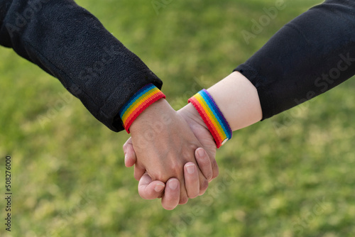 two lesbian girlfriends holding hands wearing LGBT rainbow wristbands