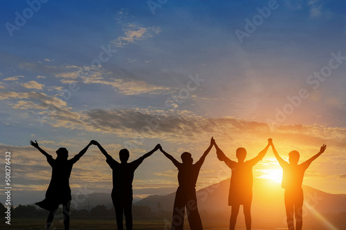 Silhouette of happy business teamwork making high hand over head standing back side on sunrise background,friendship,victory,cooperation,achievement,copy space.
