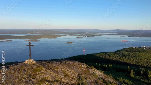 Forward reveal drone shot of orthodox cross on the top of Krestovaya mount and Kandalaksha gulf of White sea on sunny summer day. Murmansk Oblast, Russia. photo