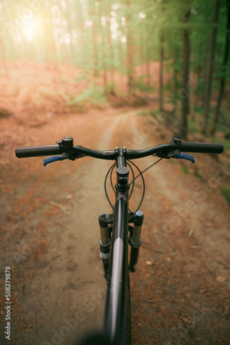 Mountain bike handlebar viewed from the first-person perspective. visible bicycle frame and bicycle accessories on the handlebar and the forest trai. Concept of spending time outdoors while bikeriding © AlexGo
