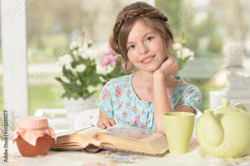 little cute girl reading book at the table at home