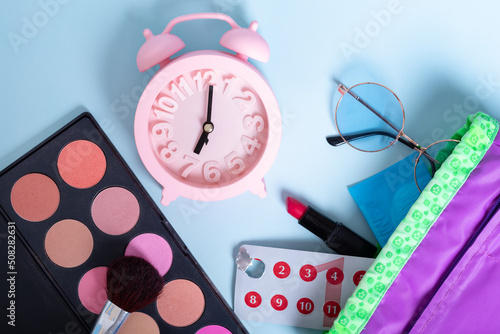 Travel makeup bag with blush, eye shadow, brush, sunglasses, lipstick, pills and a pink alarm clock as a symbol of time. Hygienic protection for women on critical days. Travel concept