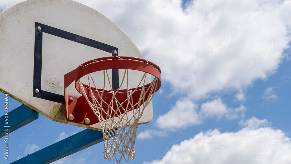 Close-up of a basketball hoop, red, in the open air, the blue sky with fluffy clouds in the background.
