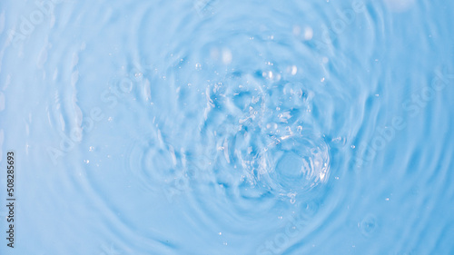 Drops fall down into clear fresh water on light blue background view from above