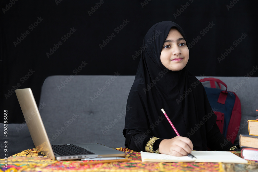 cute muslim girl writing on notebook, using a laptop computer and online learning at home cute muslim girl writing on notebook, using a laptop computer and online learning at home