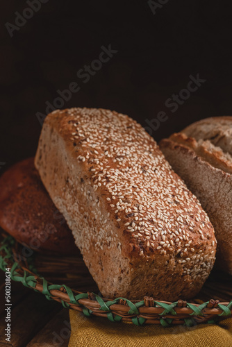 Fresh whole grain bread with sesame seeds in a basket on a dark background.
