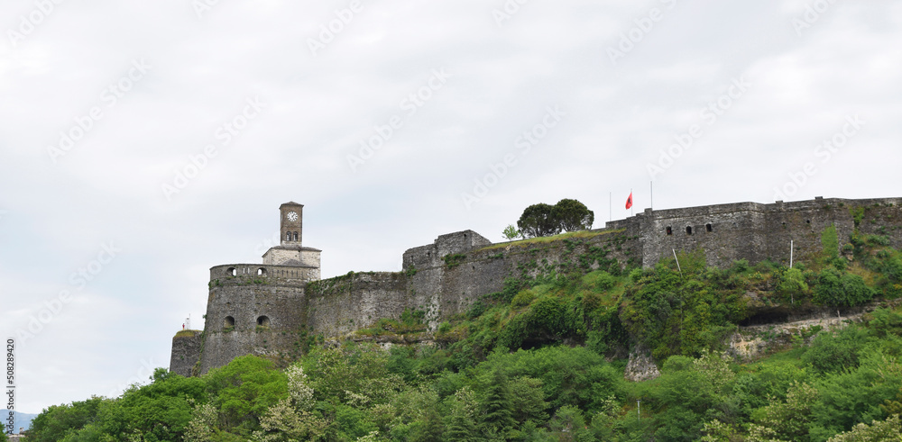 View from the city to the fortress walls and the clock tower of the Gjirokastra castle against the backdrop of the mountains in Albania
