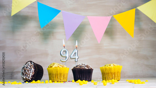 Birthday background with number 94. Beautiful birthday card with colorful garlands, a muffin with a candle burning copyspace.