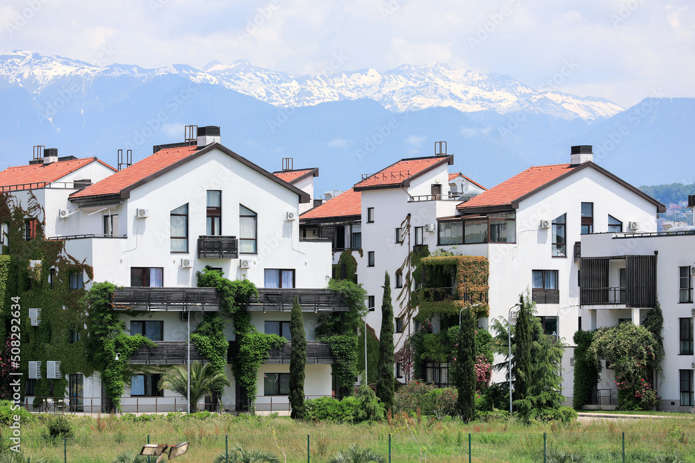 Beautiful bungalows, covered with greenery, against the backdrop of mountains and snow-capped peaks. Urban landscape. A modern beautiful city. Sochi, Russia.