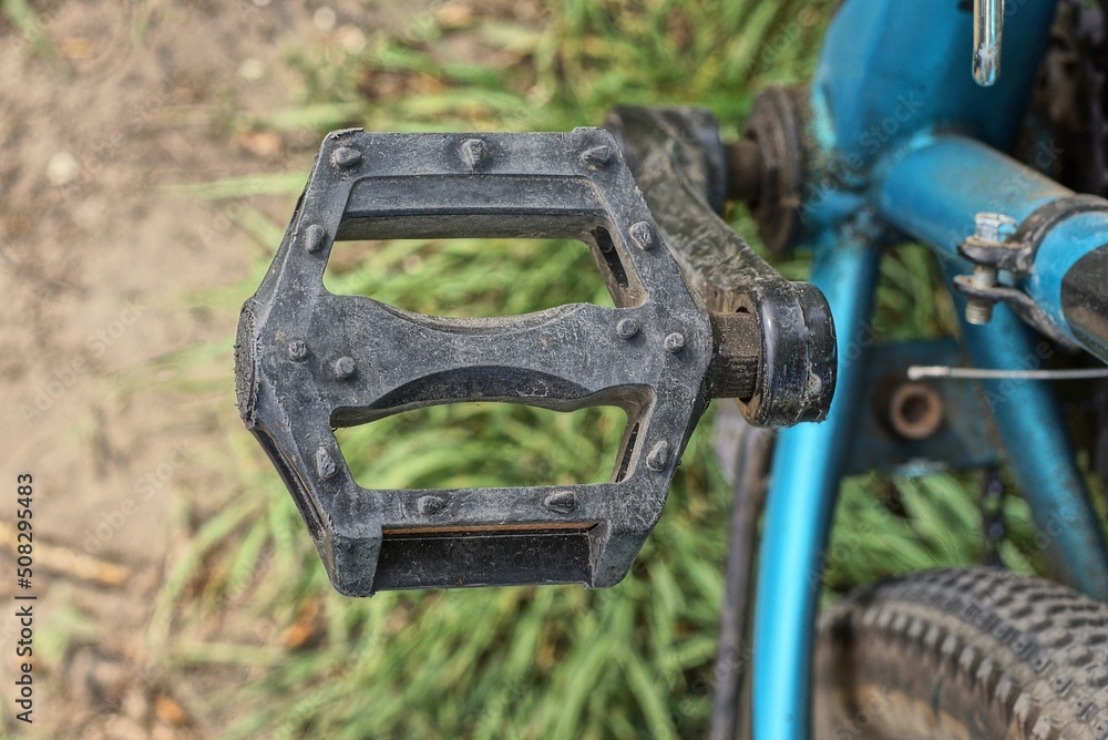 one black pedal on a blue bicycle on the background of green grass on the street