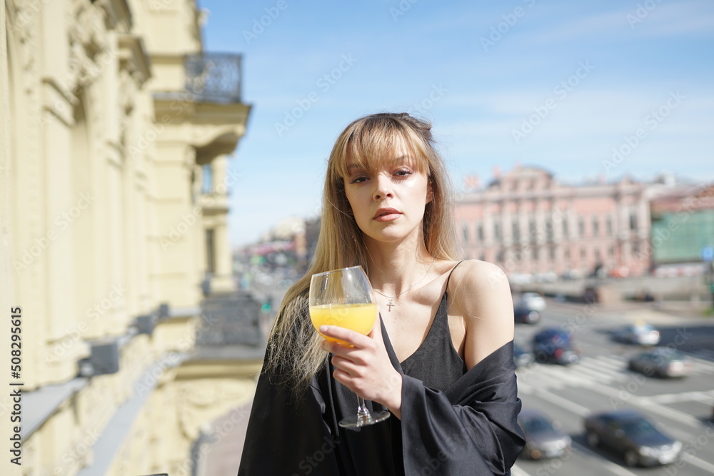 In the afternoon, in the light of the sun, a touching girl in black pajamas enjoys a glass of orange juice. She's good on the balcony. In the afternoon, in the light of the sun, a touching girl in black pajamas enjoys a glass of orange juice. She's good on the balcony.