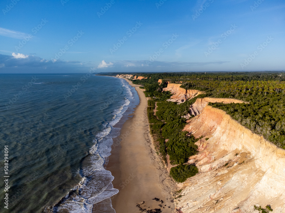 Amazing land cliffs with the golden hour of the rising sun and beautiful beach in Parrancho, Arraial da Ajuda, Bahia, Brazil, South America. Aerial drone view.