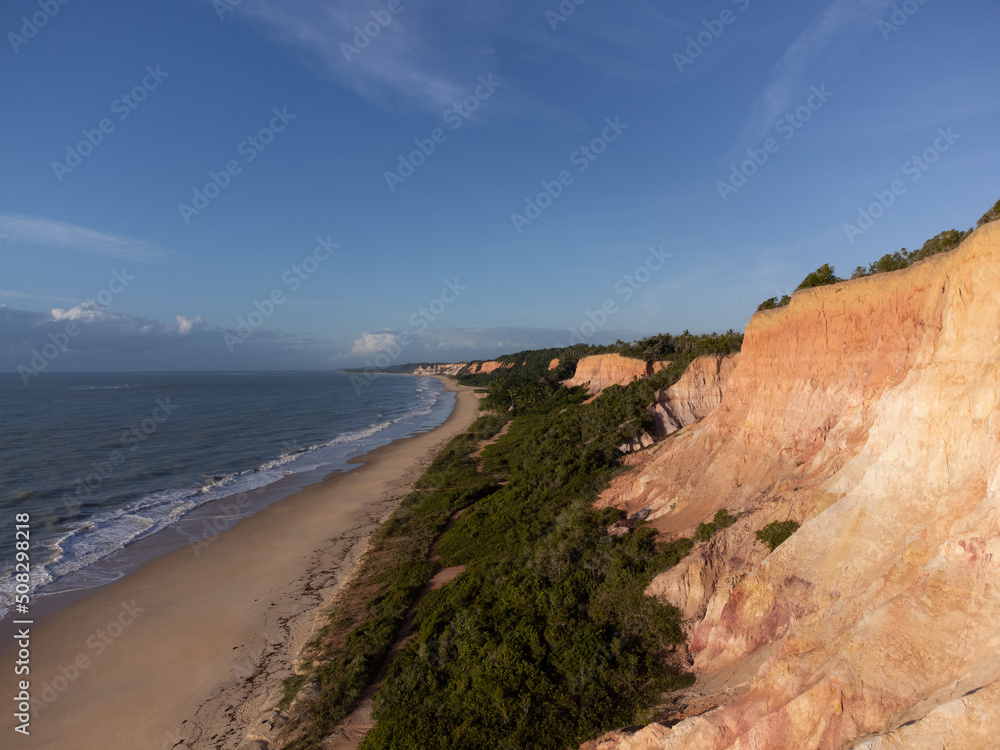 Amazing land cliffs with the golden hour of the rising sun and beautiful beach in Parrancho, Arraial da Ajuda, Bahia, Brazil, South America. Aerial drone view.