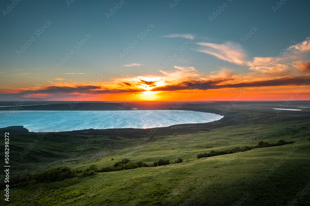 Fototapeta premium picturesque lake surrounded by a green meadow in the rays of the setting sun
