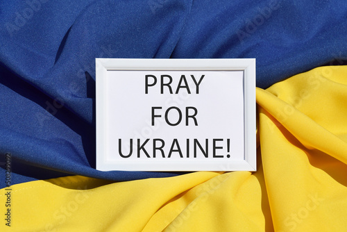 The inscription PRAY FOR UKRAINE against the background of the state flag of Ukraine, UA. photo