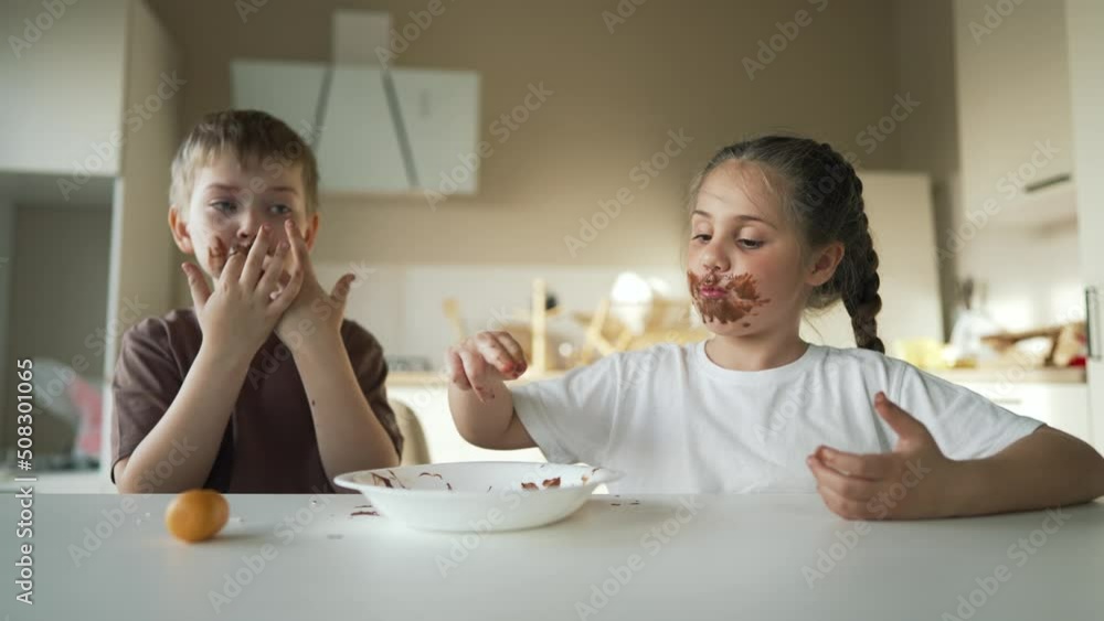 Child children eat sweet chocolate at table. Dirty face child mouth biting cocoa chocolate with teeth. Sweet breakfast of children at the table in kitchen. Happy kids with messy face eating chocolate Child children eat sweet chocolate at table. Dirty face child mouth biting cocoa chocolate with teeth. Sweet breakfast of children at the table in kitchen. Happy kids with messy face eating chocolate