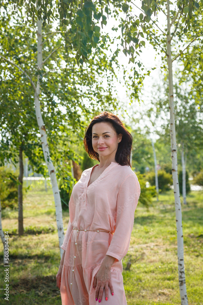 Woman in pink dress standing among green birch trees. Woman in pink dress standing among green birch trees.