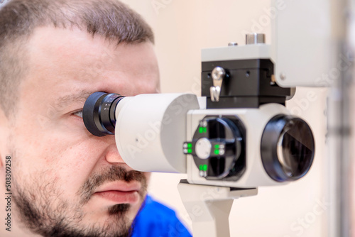 Fototapeta Naklejka Na Ścianę i Meble -  A male ophthalmologist checks a patient's vision with a modern device with a light beam