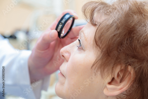 A male ophthalmologist checks the eyesight of an adult woman with a binocular ophthalmoscope photo