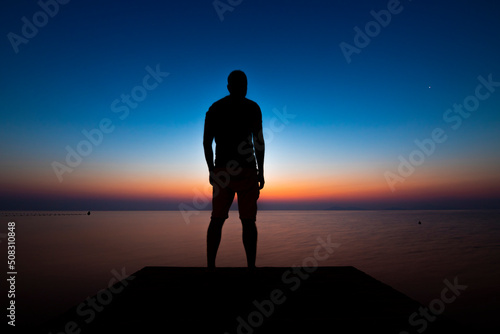 Silhouette of young man on a jetty in front of the Mar Menor, in the Region of Murcia, Spain, in a colorful sunset