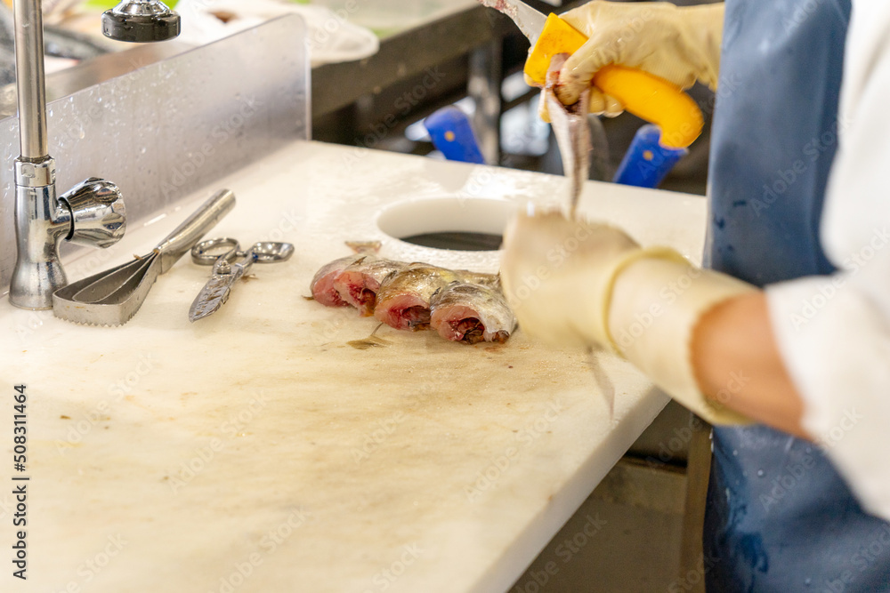 Unrecognizable fishmonger cutting fish with a knife on a white table next to the cutting utensils. High quality photo Unrecognizable fishmonger cutting fish with a knife on a white table next to the cutting utensils. High quality photo