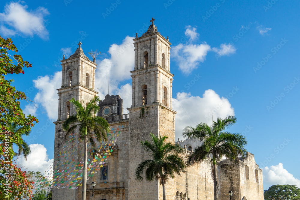 Old catholic church built in colonial style. Stone cathedral against a clear blue sky. Spanish Cathedral with palm trees in the courtyard, decorated with flags.