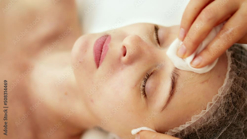 Beautician cosmetologist cleanses the skin of face using napkins before professional cosmetic procedure in a beauty clinic salon for client. Skincare and cosmetology spa concept. Beautician cosmetologist cleanses the skin of face using napkins before professional cosmetic procedure in a beauty clinic salon for client. Skincare and cosmetology spa concept.