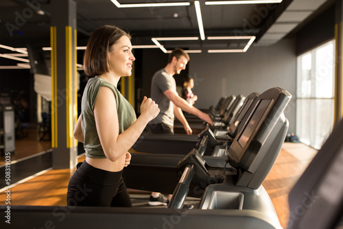 Row of young people running on treadmills in modern sport gym