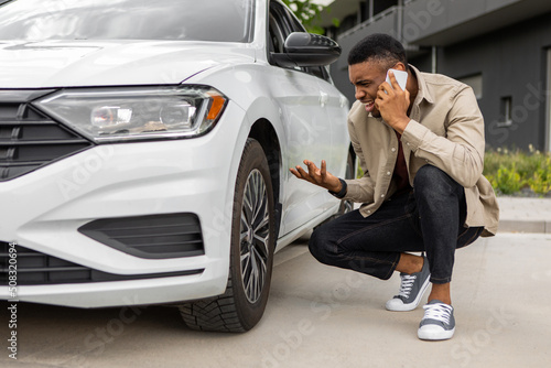 Young man sitting near broken car and calling to car service.  © Home-stock