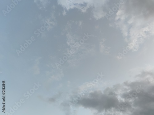 Light sky with clouds. Under a bright white sky with high solid clouds, rare white-gray cumulus clouds hang low. They have different shapes and sizes.