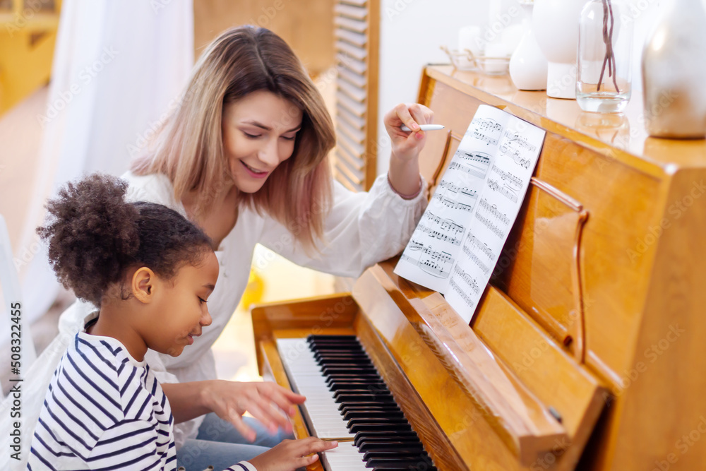 Foto Stock Woman and girl playing a piano. Beautiful mom teaching her
