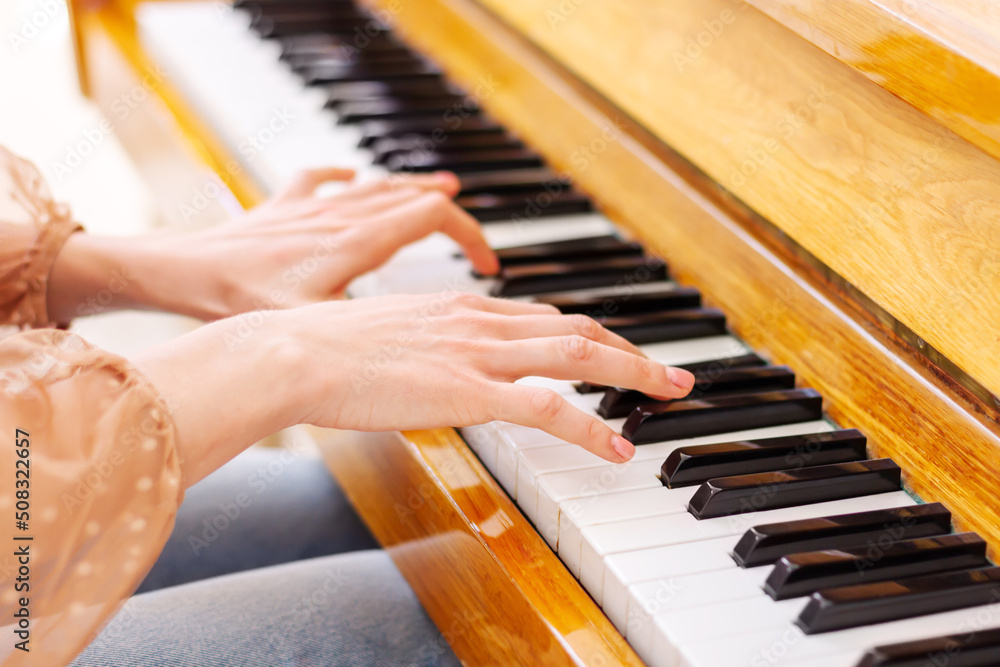 Fototapeta premium Close up of hands young talented woman playing the piano at home, performing classical music, getting ready to the classes in the music school. Musical artist create instrumental acoustic melody.