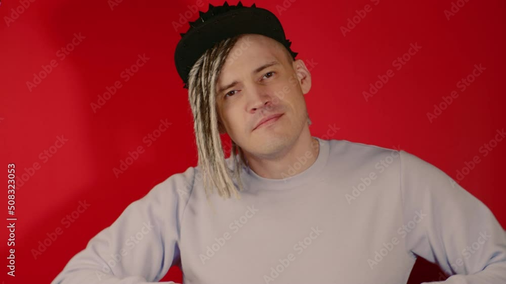 Young handsome cheerful man in black cap dancing, snapping fingers. Stylish guy with blonde dreadlocks having fun, dancing with good mood on red background. Young handsome cheerful man in black cap dancing, snapping fingers. Stylish guy with blonde dreadlocks having fun, dancing with good mood on red background.
