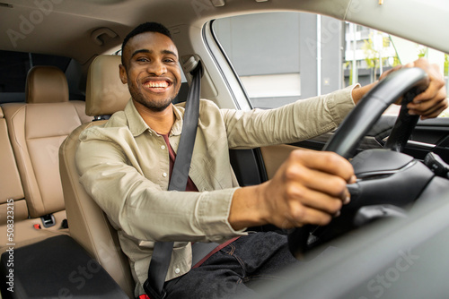 African American driver with hands on steering wheel looking at camera