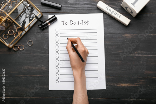 Konstfotografi Female hand with to-do list, cosmetics and accessories on dark wooden background