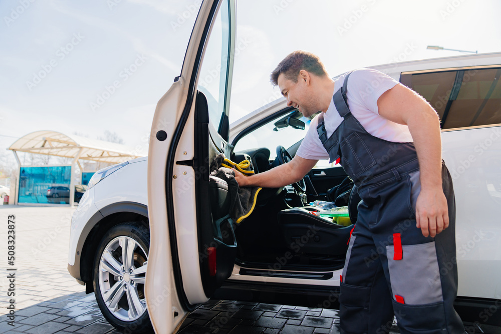 self-service car wash. man in work jumpsuit wipes car cabin dry after washing self-service car wash. man in work jumpsuit wipes car cabin dry after washing