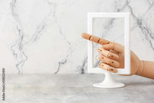 Wooden hand pointing through frame on light background