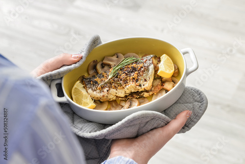 Woman holding baking dish with tasty sea bass fish in kitchen photo