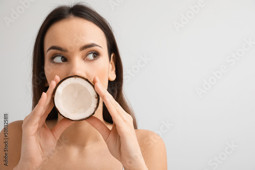 Pretty young woman with coconut on light background