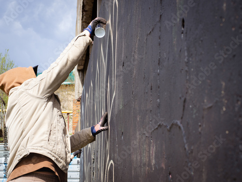 guy in a hood and black glasses writes graffiti