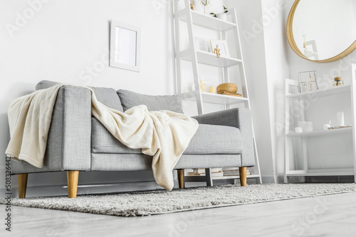 Grey sofa with plaid, mirror and shelving units in light living room photo